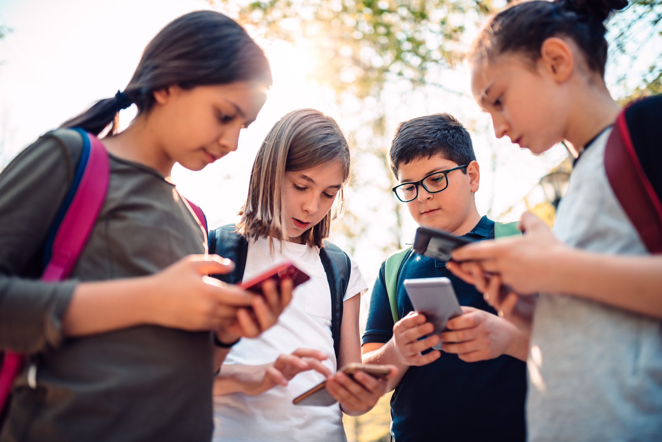 Kids standing next to each other but staring at their smart phones after school
