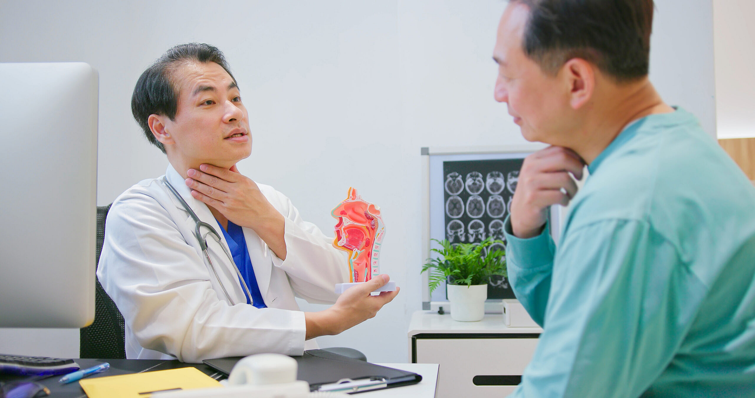 Male doctor talking to a patient and holding his throat to explain the problem